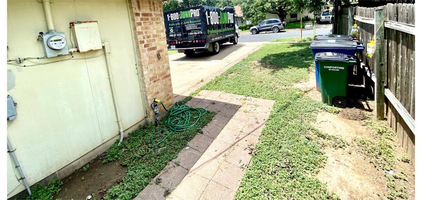 After: the same narrow side yard cleared to bare ground and grass, only a coiled garden hose left by the wall.