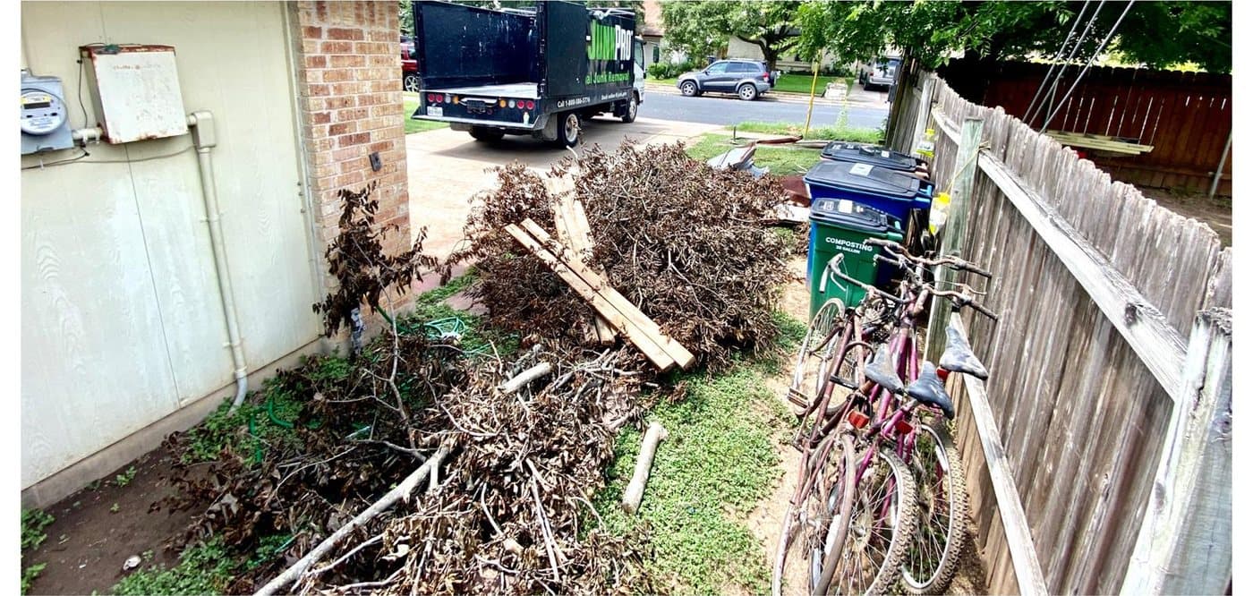 Before: a pile of dead brush and cut lumber against a house wall, bikes and trash bins lined up along the wooden fence beside it.
