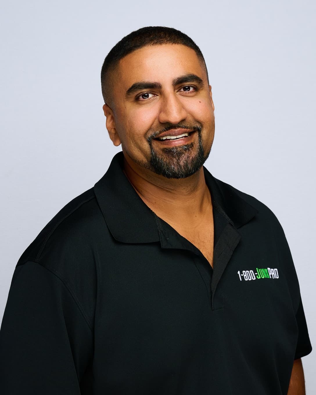 Tariq Zuhair smiling in a black 1-800-JUNKPRO polo shirt.