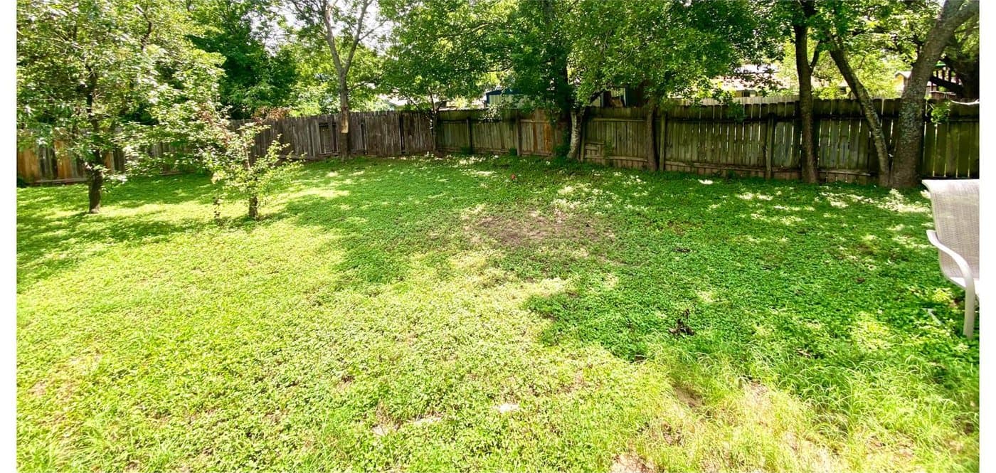After: the same backyard open and mowed, trampoline and branch piles gone, just grass to the fence line.