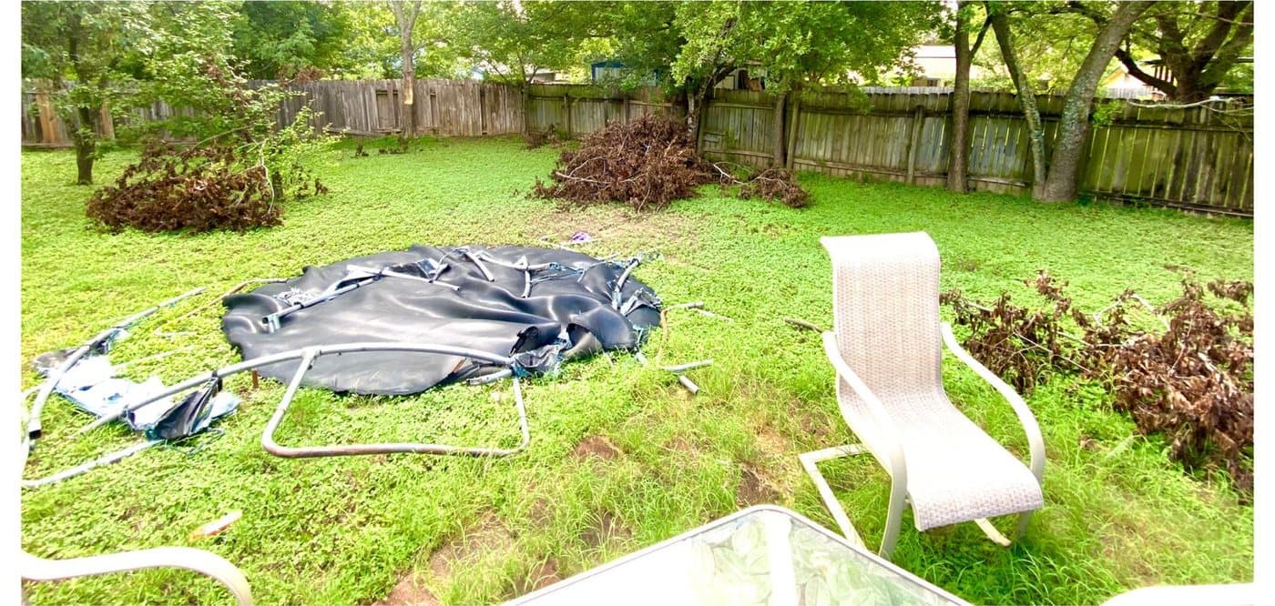 Before: a collapsed trampoline frame and torn mat lying in tall grass next to piles of dead tree branches.